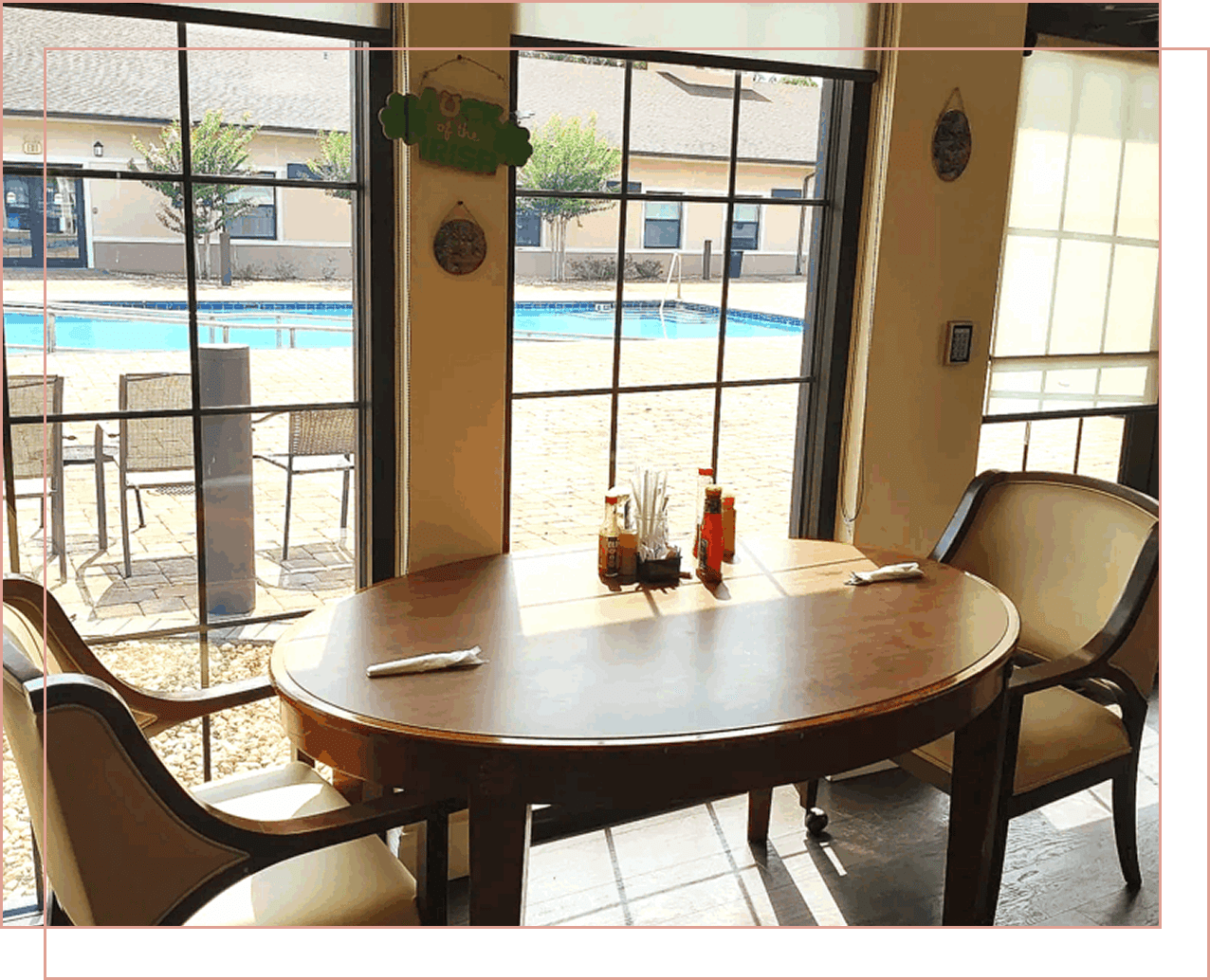 Cozy table by large windows overlooking a sunny pool area.