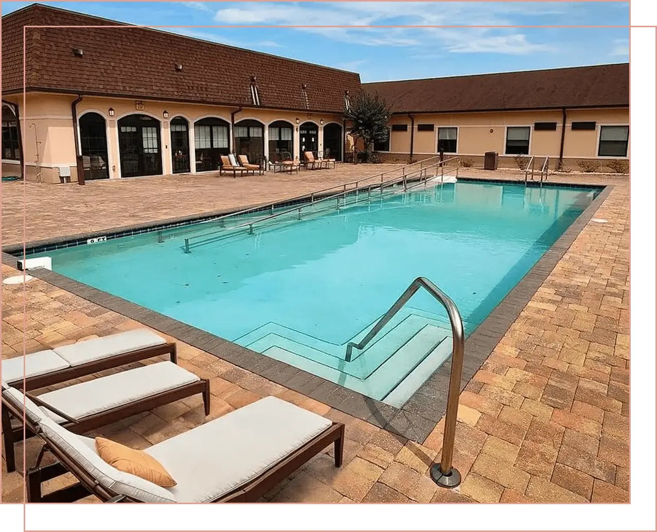 Outdoor pool area with lounge chairs and clear blue water under a partly cloudy sky.
